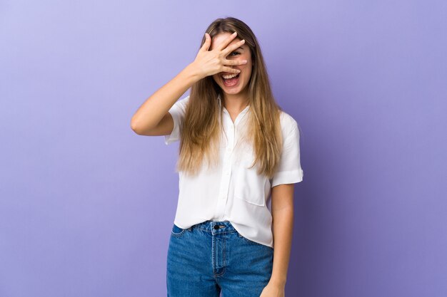 Young woman over purple wall covering eyes by hands and smiling