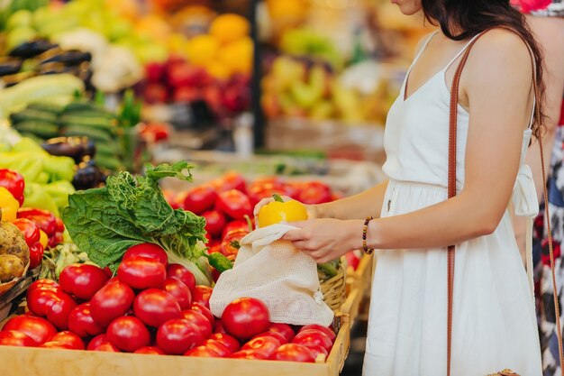 Young Woman puts fruits and vegetables in cotton produce bag at food market. Reusable eco bag for shopping. Zero waste concept.