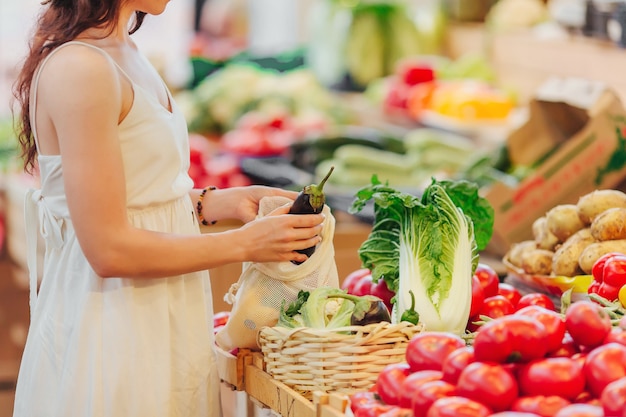 Young Woman puts fruits and vegetables in cotton produce bag at food market. Reusable eco bag for shopping. Zero waste concept.