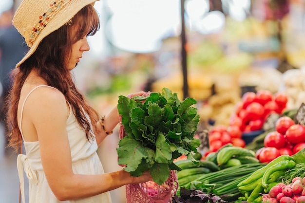 Young Woman puts fruits and vegetables in cotton produce bag at food market. Reusable eco bag for shopping. Zero waste concept.