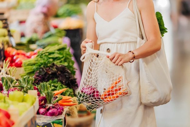 Young Woman puts fruits and vegetables in cotton produce bag at food market. Reusable eco bag for shopping. Zero waste concept.