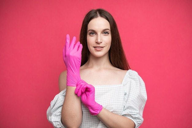 Young woman puts on protective surgical sterile gloves on her arm, isolated on pink background