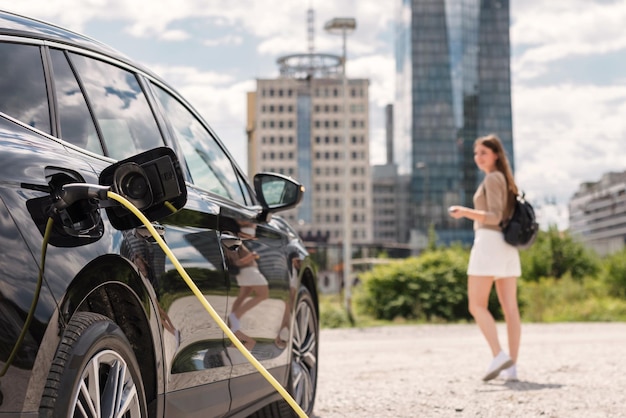 Young woman putting a charger in an electric car in a parking lot locking it remotely while moving