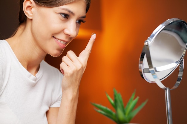 Young woman putting contact lens in her eye close up