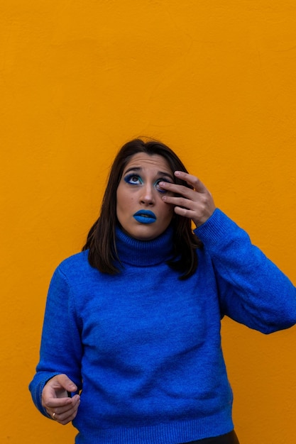 Young woman putting contact lens in her eye on vertical orange background