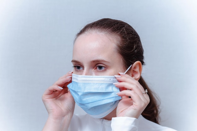 Young woman putting on face mask on a gray background Caucasian female adjusts the protective mask with her hands