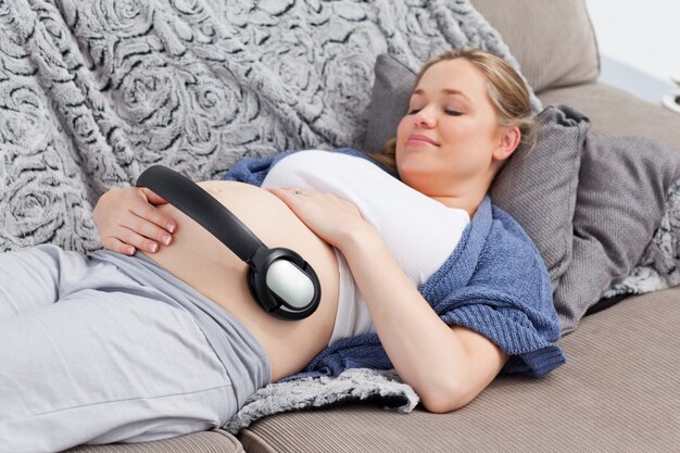 Young woman putting her earphones on her belly 