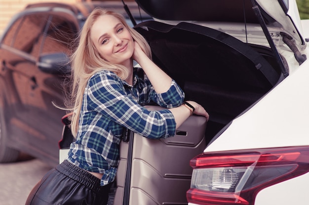 A young woman putting her luggage in the trunk of a car