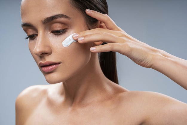 Young woman putting moisture cream on cheeck