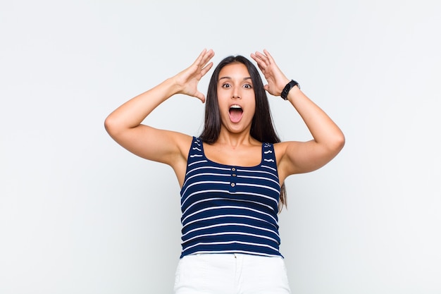 Young woman raising hands to head, open-mouthed, feeling extremely lucky, surprised, excited and happy