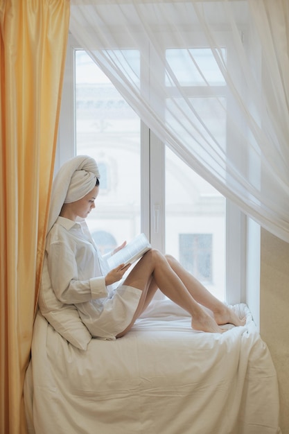 Young woman reading a book beside the window after get up in the morning Morning lifestyle concept