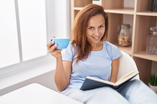 Young woman reading book and drinking coffee at home