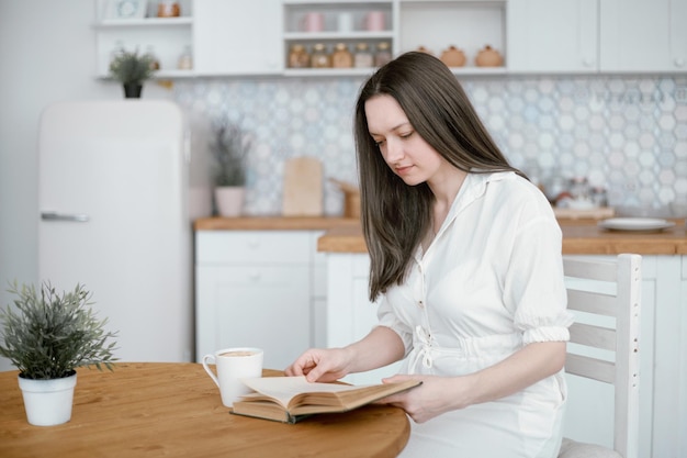 Young woman reading a book sitting at the kitchen table