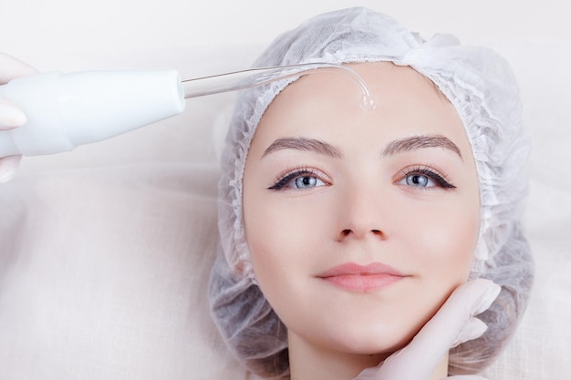 Young woman receiving electric darsonval facial massage after procedure at beauty room close up