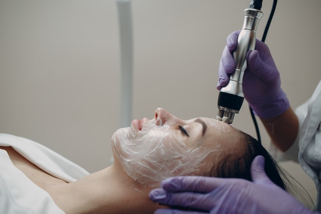 Young woman receiving electric RF lifting facial massage at beauty spa with electroporation equipment.