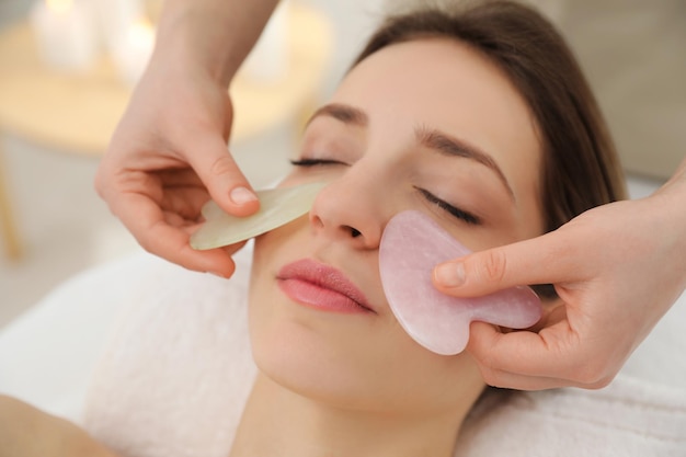 Young woman receiving facial massage with gua sha tools in beauty salon closeup