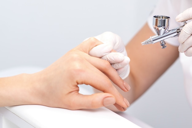 Young woman receiving manicure by airbrush in nail salon. Procedure for spraying paint on the nails