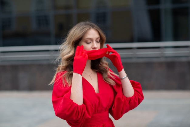 Young woman in red dress and gloves puts on medical facemask