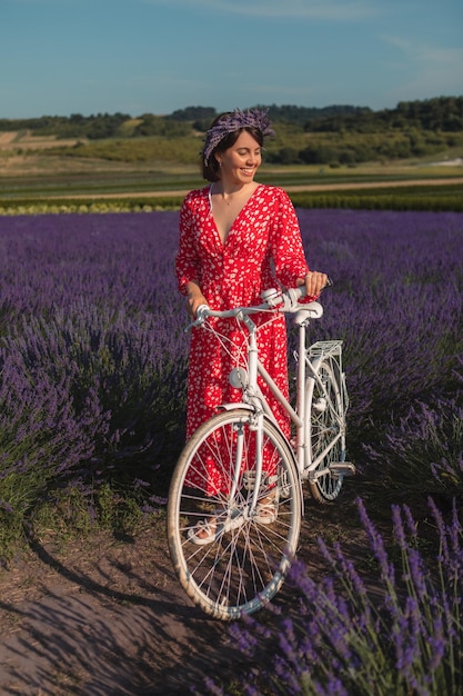 A young woman in a red dress stands with a bicycle in a lavender field