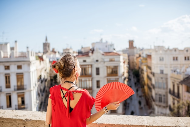 Young woman in red dress with hand fan and photo camera enjoying beautiful cityscape view on Valencia city during the sunny weather in Spain