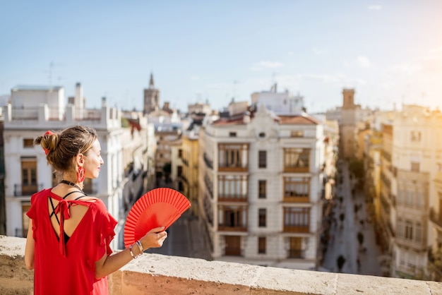 Young woman in red dress with hand fan and photo camera enjoying beautiful cityscape view on Valencia city during the sunny weather in Spain