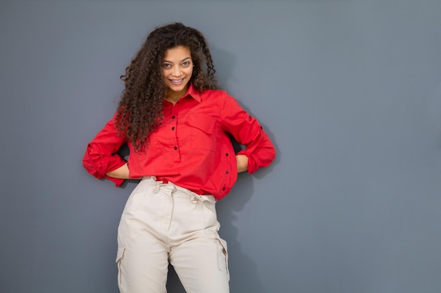 Young woman in red shirt standing against grey wall