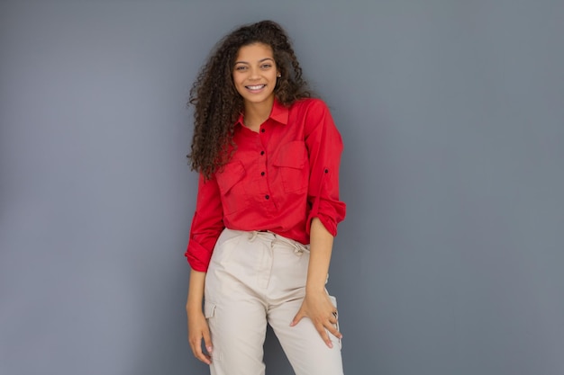 Young woman in red shirt standing against grey wall