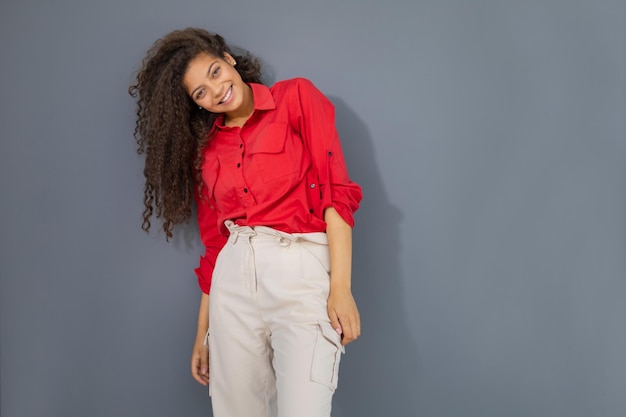 Young woman in red shirt standing against grey wall