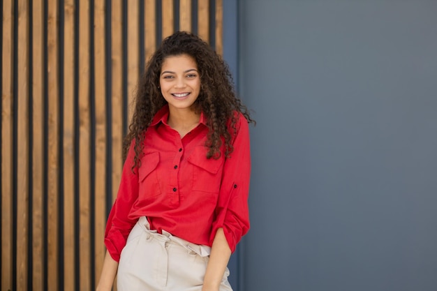 Young woman in red shirt standing against grey and wooden wall