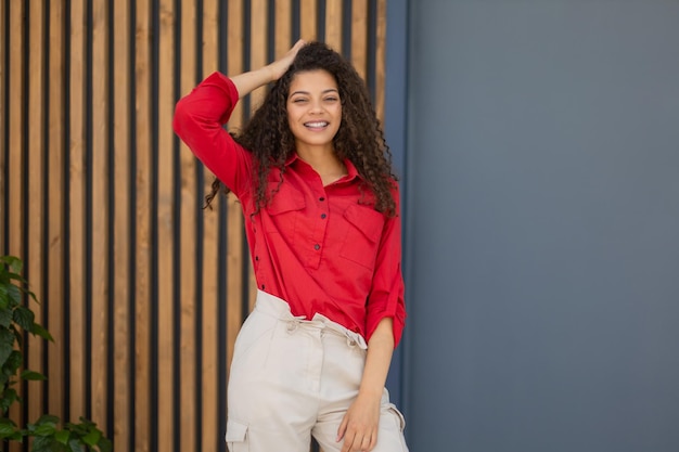 Young woman in red shirt standing against grey and wooden wall