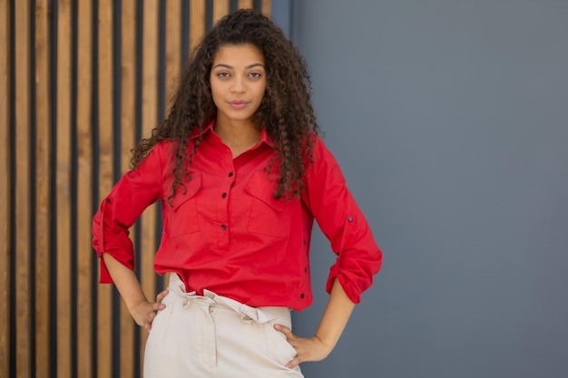 Young woman in red shirt standing against grey and wooden wall