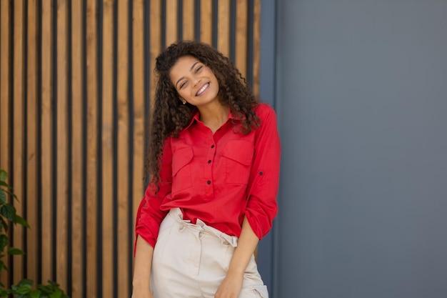 Young woman in red shirt standing against grey and wooden wall