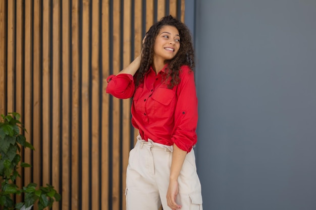 Young woman in red shirt standing against grey and wooden wall