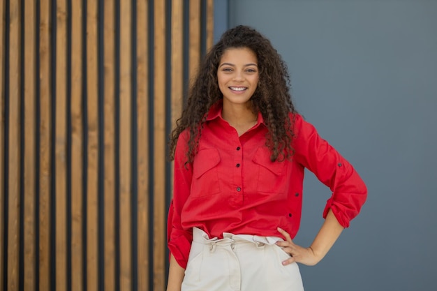 Young woman in red shirt standing against grey and wooden wall