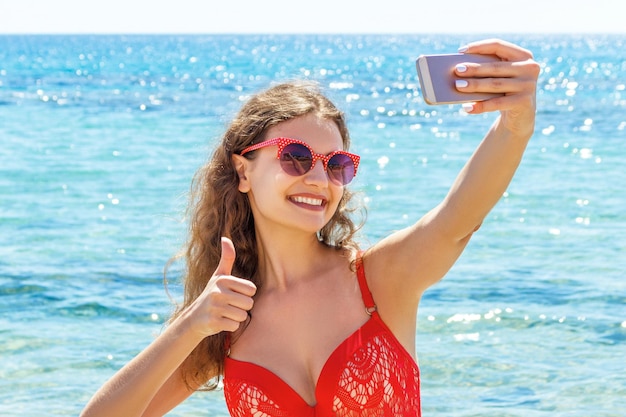 Young woman in red swimsuit is taking selfportrait at the sea background Beach concept