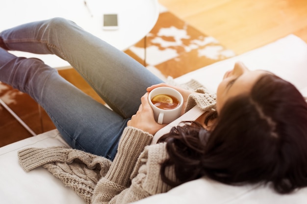 Young woman relaxing on sofa holding cup with lemon tea