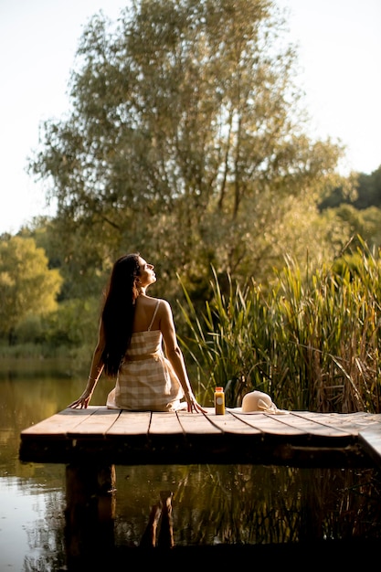 Young woman relaxing on the wooden pier at the calm lake on a hot summer day