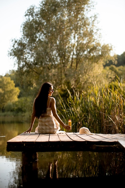 Young woman relaxing on the wooden pier at the calm lake on a hot summer day