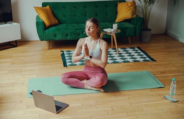 Photo young woman relaxing on a yoga mat in front of a laptop on a hardwood floor