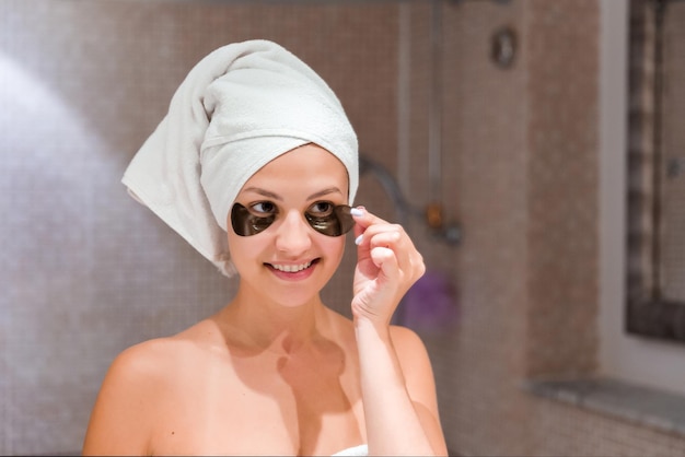 Young woman removes undereye patches looking in mirror at home in bathroom Beauty skincare and wellness morning concept