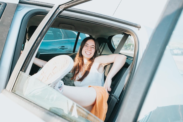 Young woman resting on the back seats of a car smiling during a sunny day