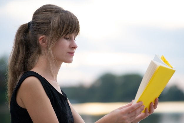 Young woman resting in summer park reading a book. Education and sudy concept.