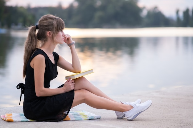 Young woman resting in summer park reading a book. Education and sudy concept.