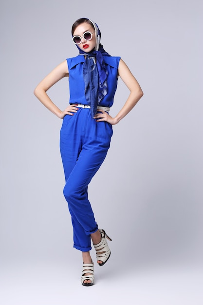 Young woman in retro style with sunglasses and silk scarf and blue overalls. Sixties style fashion retro woman.