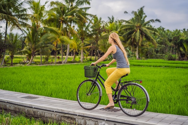 A young woman rides a bicycle on a rice field in Ubud Bali Bali Travel Concept