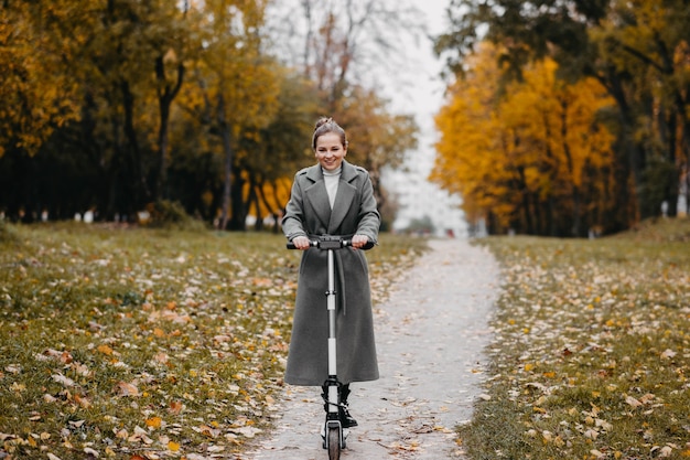 young woman riding an electric scooter in a city park in autumn