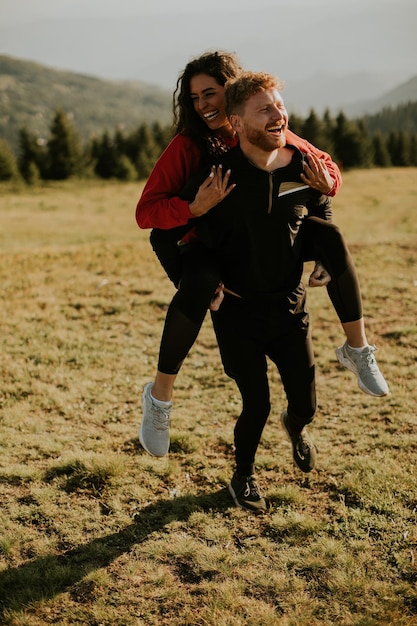 Young woman riding piggyback on a boyfriend at green hills