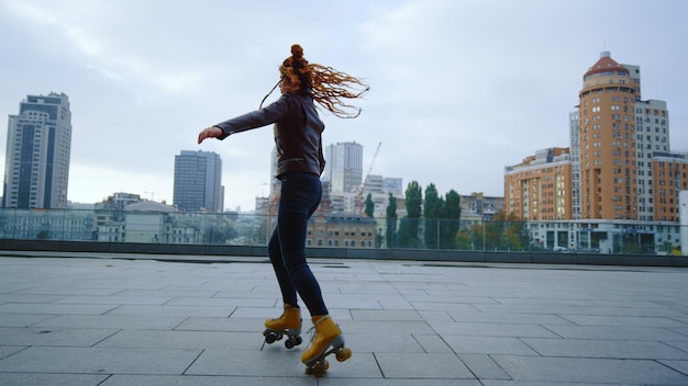 Young woman riding on roller skates on urban background Sporty hipster girl performing elements of rollerblading outdoor Active roller skater dancing outside Street sports concept