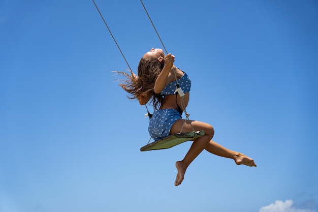 Young woman on the rope swing with blu sky background concept of individuality creativity