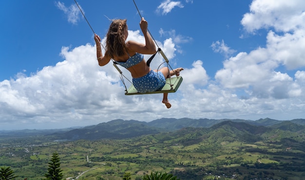 Young woman on the rope swing with sky and mountains background concept of freedom and happiness